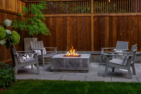 Outdoor fireplace lit at dusk with Adirondack seating