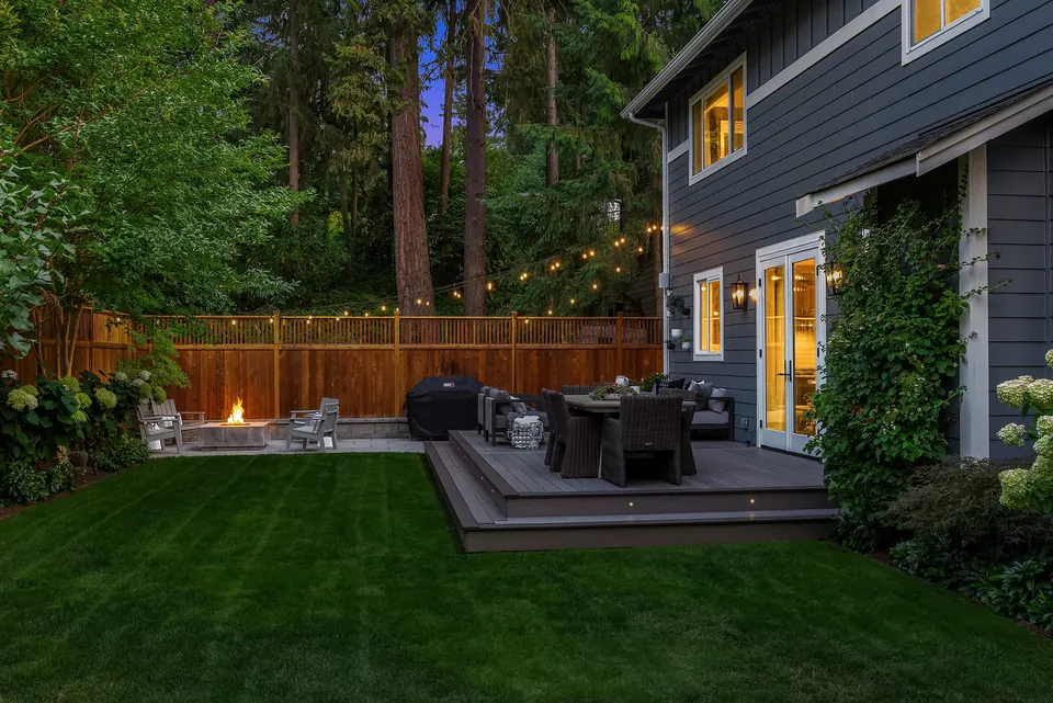 Rebuilt backyard at dusk with lawn, composite deck, and a lit fire pit beside the house
