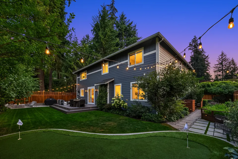 Back of the home at dusk with string lights, putting green, and glowing windows