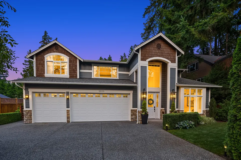 Front of the home at dusk with warm window light, covered entry, and three-car garage