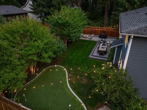 Aerial view of the backyard at dusk showing putting green, deck, and cafe lights